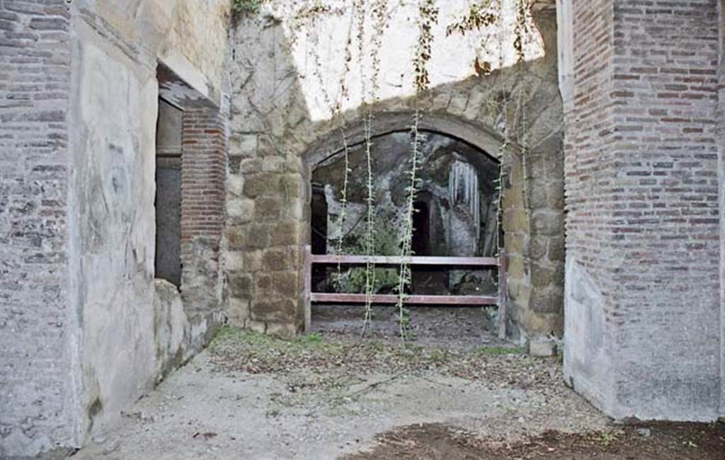 II.2 Herculaneum, October 2001. 
Looking west through doorway from west portico towards the site of a Bourbon tunnel, with column visible.
On the left would be other living room, bedrooms and a terrace overlooking the sea, none of which are accessible. 
On the right is a second smaller peristyle garden. Photo courtesy of Peter Woods.
According to Bonucci (April 1828) –
“Uno de’ portichetti descritti, il solo finora scoverto, vien formato da tre colonne doriche di mattoni rivestiti di stucco (Tav. XII, no.5).
Nell’angolo v’ ha un bel pilastro dipinto di rosso (Tav. XII, no.6). Fra gli intercolunnj si estende un picciolo poggio animato da figurine d’uccelli e di fiori. 
I capitelli sono abbelliti da qualche rara foglia d’acanto e da qualche minuto ma grazioso ornamento. Essi sostengono un ferro orizzontale da cui doveano pendere ricchi drappi che costavano prezzi enormi e che venivano sovente ricamati e varj colori………………………
Ecco cio che gli scavamenti ulteriori ci faranno conoscere. 
Per un tale oggetto bisognera introdursi al di sotto della strada moderna (Tav. XII, no.5, 25) e sfidare de’ travagli che non si potrebbero apprezzare abbastanza. Ma se l’incoraggiamento e l’approvazione dell’Accademia non mi manchera nella mia onorevole ma penosa carriera, io non temero di penetrare ove fara d’uopo……….”  Bonucci.”
(One of the porticoes described, the only one so far excavated, is formed by three Doric columns of bricks covered with stucco (Tav. XII, no.5). 
In the corner there is a beautiful pillar painted red (Tav. XII, no.6). Between the columns extends a small wall animated by figurines of birds and flowers. The capitals are embellished with some rare acanthus leaf and a few small but graceful ornaments. They support a horizontal iron from which rich drapes would have hung, and that were often embroidered and in various colours........................... 
Here then is what the further excavations will let us know. In order to achieve this, it will be necessary to enter below the modern road (Tav. XII, no.5, 25) and trust to the work that cannot be appreciated enough. But if the encouragement and approval of the Academy will not be lacking in my honorable but painful career, I will not be afraid to penetrate where it will be necessary.......... Bonucci.)
See Ruggiero, M. (1885). Storia degli scavi di Ercolano ricomposta su’ documenti superstiti. (p.549).


