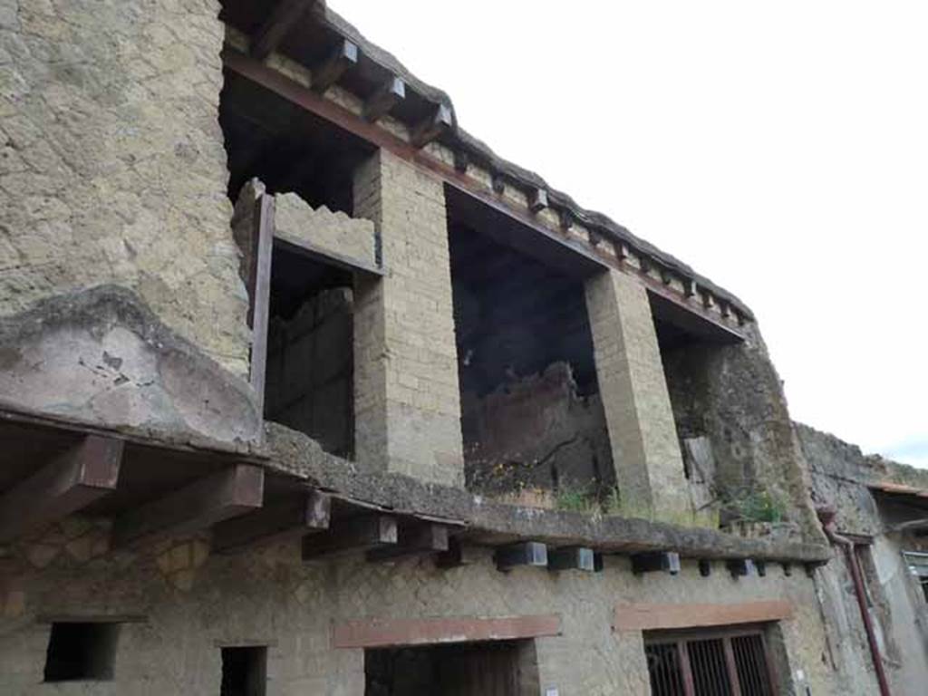 V.7 Herculaneum. May 2010.  Upper floor of House of Neptune and Amphitrite above entrance doorway, looking south-east from Cardo IV Superiore. According to Maiuri, the outside wall of the upper storey was overthrown either by the earthquake accompanying the eruption or by the onslaught of the lave-flow.
This means that now the interior of the rooms of the living quarters overlooking the street, can be seen from the street. The partition walls are still well decorated. 
There is a cubiculum which had a wooden bedstead, a candelabrum and a marble monopod (table support).
See Maiuri, Amedeo, (1977). Herculaneum. 7th English ed, of Guide books to the Museums Galleries and Monuments of Italy, No.53 (p.43).
