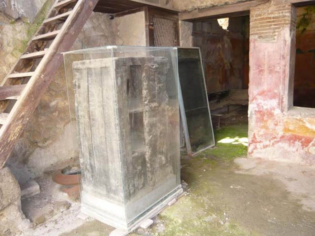 V 17, Herculaneum, Herculaneum. May 2009. Looking towards east side with remains of a cupboard/wardrobe. Photo courtesy of Buzz Ferebee. 
In the space under the steps can be seen a dolium buried into the ground, and nearby was a terracotta oven. On the left through the doorway to the rear room, the remains of a carbonized wooden bed can be seen.

