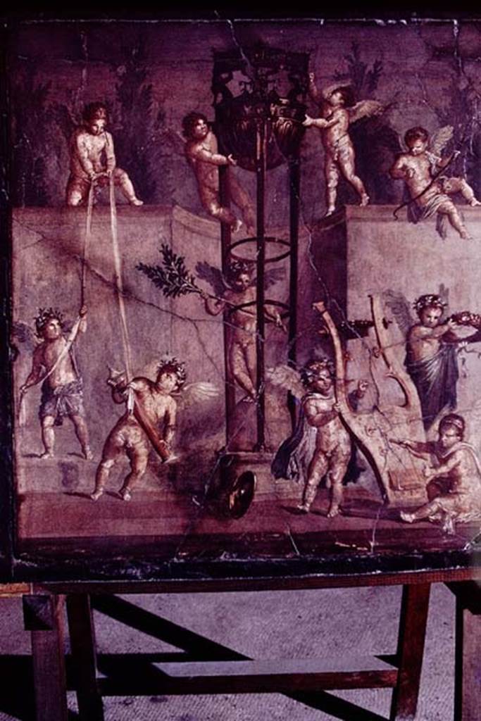 V.18/17, Herculaneum, 1978. Painting of cupids playing with the attributes of Apollo including a tripod, found in the centre of the north wall in an upper room.
Photo by Stanley A. Jashemski.   
Source: The Wilhelmina and Stanley A. Jashemski archive in the University of Maryland Library, Special Collections (See collection page) and made available under the Creative Commons Attribution-Non Commercial License v.4. See Licence and use details.
J78f0501
According to Esposito, this painting was found in the centre of the north wall in “Bottega V.17, ambiente (18)”.
See Esposito, D. (2014). La pitture di Ercolano. Rome, “L’Erma” di Bretschneider, (tav.74) in Studi della Soprintendenza archeologica di Pompei, no.33.
According to Pagano and Prisciandaro, painted plaster was found on 21st December 1937 in an upper room.
Now in Naples Archaeological Museum, inventory number 149336.
21 dic 1937 Ercolano. 
Piano superiore, intonaco dipinto: “abaco di intonaco incassato nella cornice di legno originaria (carbonizzata) nel quale sono degli eroti che giocano col tripode apollineo”. (NAP 149336).
See Pagano, M. and Prisciandaro, R., 2006. Studio sulle provenienze degli oggetti rinvenuti negli scavi borbonici del regno di Napoli. Naples: Nicola Longobardi. (p.232).
