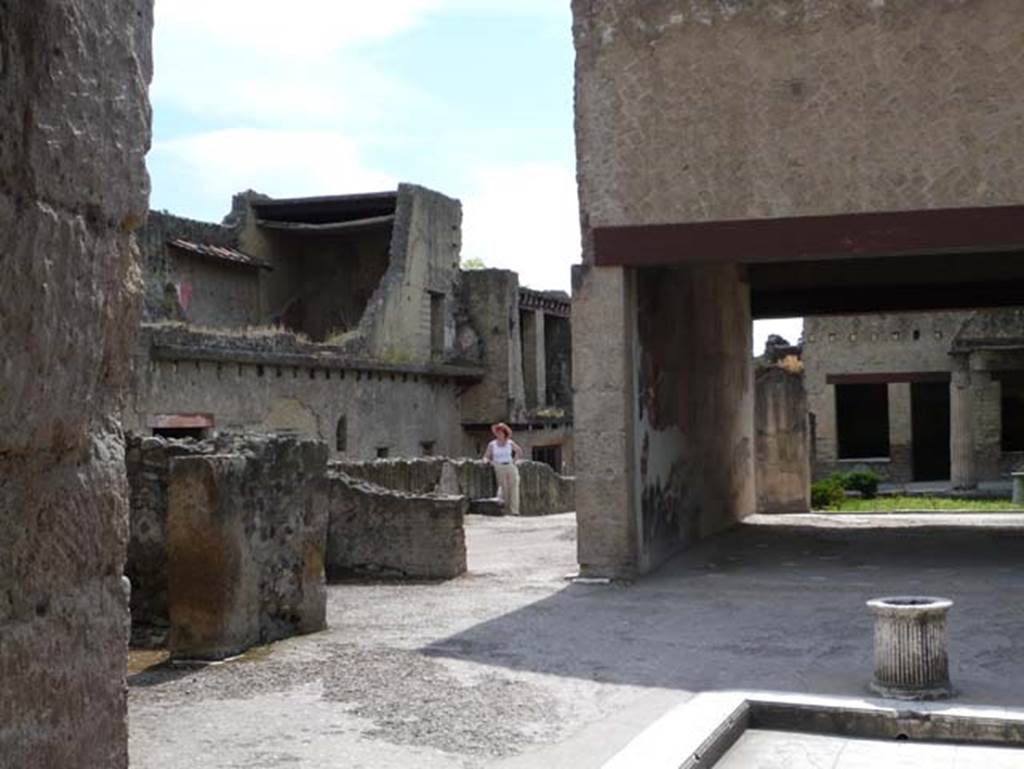 VI.13, Herculaneum, May 2009. Looking south-east across atrium towards two doorways to rooms on east side of atrium.  These would be cubiculum 5, on left, and east ala 6, By the east wall of the tablinum would have been a doorway into oecus 8, now with reduced walls where the figure is standing. Photo courtesy of Buzz Ferebee.
