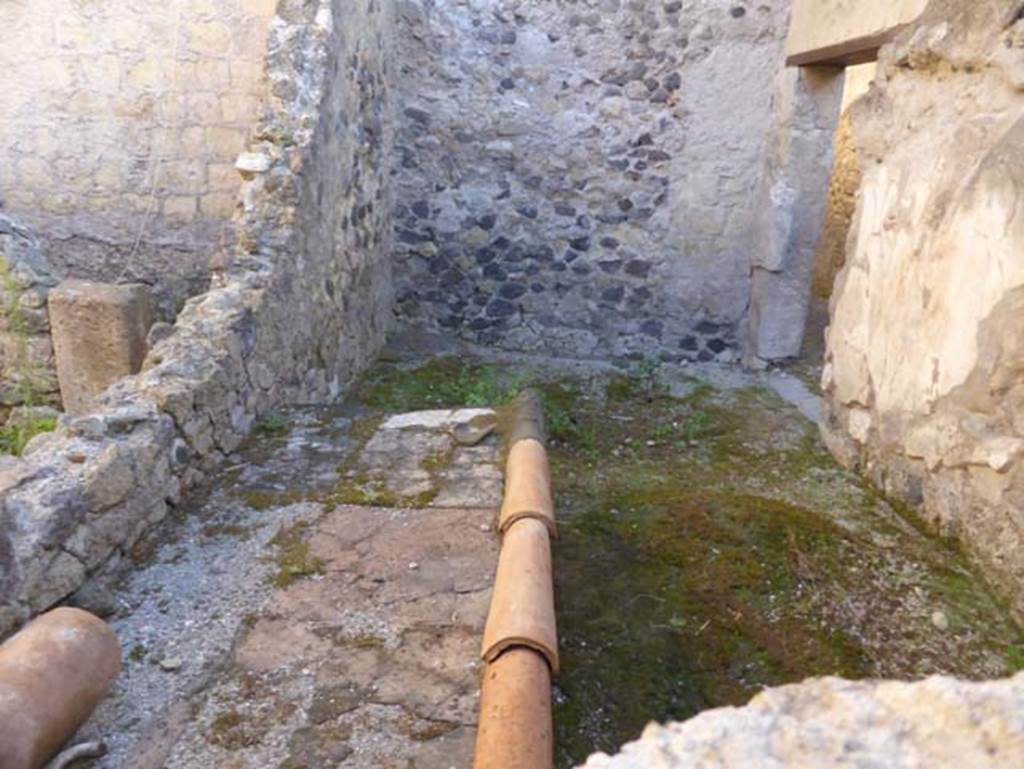 VI 26 Herculaneum, September 2015. Looking east through window into kitchen with bench and remains of lararium with painted serpents. Leaning against the north wall was a large masonry bench which was used as the kitchen. The latrine was situated in the south-west corner. The walls of the rooms were entirely in opus incertum: the west and south wall were reasonably preserved; the east wall was partly destroyed by a Bourbon tunnel, and the north wall was missing a large area above the kitchen bench. The room had flooring of simple beaten earth, and the walls were not decorated with the exception of the lararium painted on the south wall.
