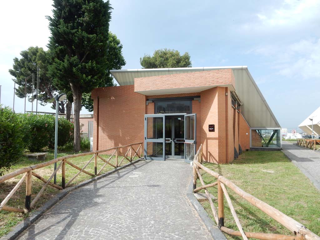 Herculaneum, June 2019. 
Entrance to boat exhibit, and other artefacts. This can be found on the south side (left) of the access roadway.
Photo courtesy of Buzz Ferebee.
