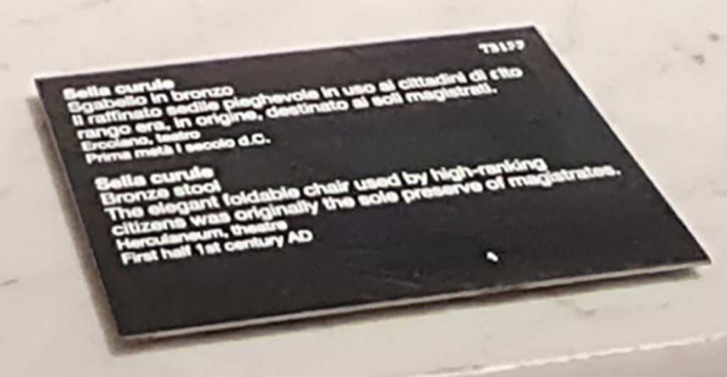 Herculaneum Theatre. April 2023. Descriptive card. Second bronze stool. Sella curule. 
Scheda descrittiva. Sella curule. Sgabello in bronzo.
Photo courtesy of Giuseppe Ciaramella.
