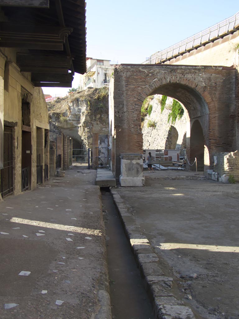 Decumanus Maximus, south side, September 2015. 
Looking west along drainage channel on the north side of Insula VI, towards the four-sided arch of the Augusteum/Basilica.
Photo courtesy of Michael Binns.
