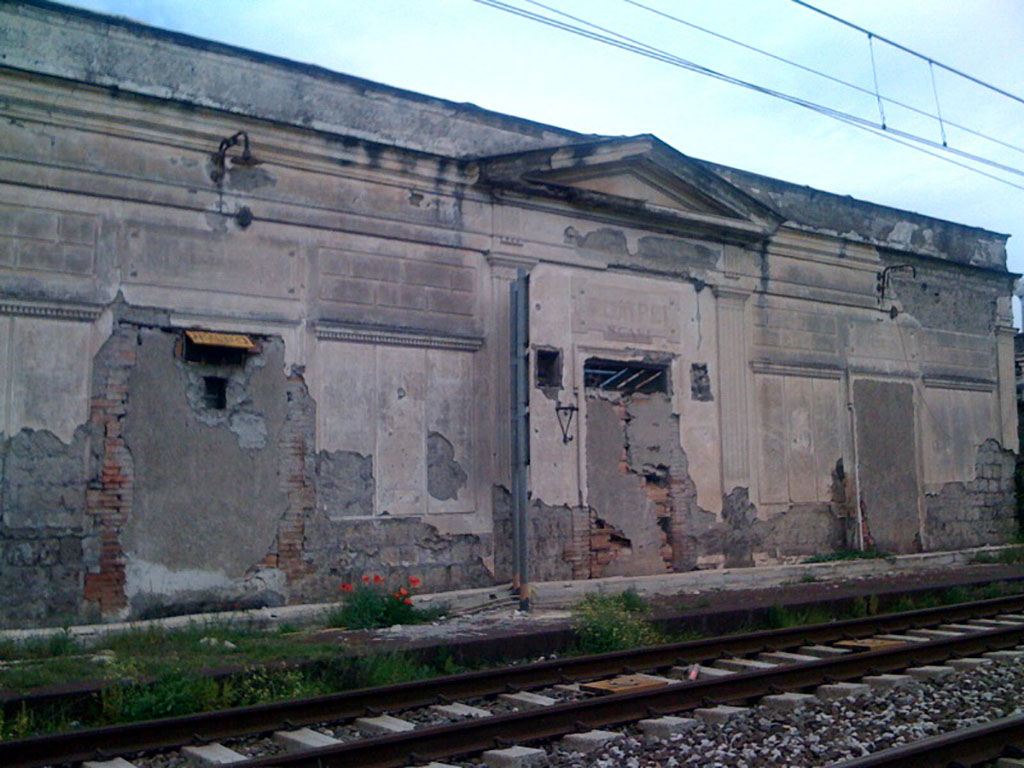 H.8. Disused Pompeii Scavi station on the line from Naples to Salerno. 2010. Photo courtesy of Rick Bauer.
Mark Twain visited Pompeii in 1867.
In his satirical account he describes leaving Pompeii: We came out from under the solemn mysteries of this city of the Venerable Past—this city which perished, with all its old ways and its quaint old fashions about it, remote centuries ago, when the Disciples were preaching the new religion, which is as old as the hills to us now—and went dreaming among the trees that grow over acres and acres of its still buried streets and squares, till a shrill whistle and the cry of “All aboard—last train for Naples!” woke me up and reminded me that I belonged in the nineteenth century, and was not a dusty mummy, caked with ashes and cinders, eighteen hundred years old. The transition was startling. The idea of a railroad train actually running to old dead Pompeii, and whistling irreverently, and calling for passengers in the most bustling and business-like way, was as strange a thing as one could imagine, and as unpoetical and disagreeable as it was strange.
See Twain M., 1869. The Innocents Abroad or the New Pilgrims Progress. Hartford, CT: American Publishing Co., Chapter XXXI.
