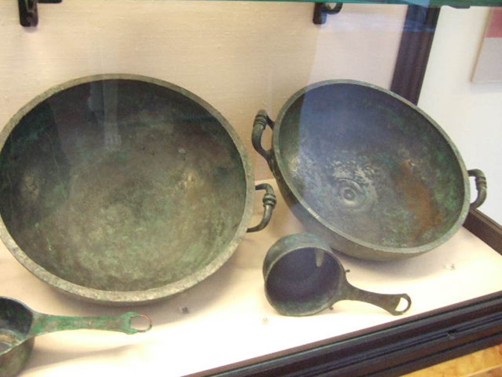 I.2.10 Pompeii.  Found in Tablinum. (left rear)  Bronze bowl.  Now in Naples Archaeological Museum. Inventory number: 111554.    (left front)  Small Bronze saucepan.  Now in Naples Archaeological Museum. Inventory number: 115975.   Found in Tablinum. (right rear)  Bronze bowl.  Now in Naples Archaeological Museum. Inventory number: 111555.  Found in Tablinum. (right front)  Small Bronze saucepan.  Now in Naples Archaeological Museum. Inventory number: 110061.

