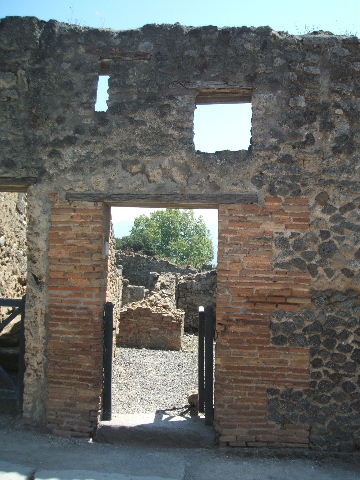 I.3.16 Pompeii. December 2007. West wall with remains of podium. This used to have two tubs at the south end. The boiler, the round gap in the centre of the picture, was used to heat a vessel.