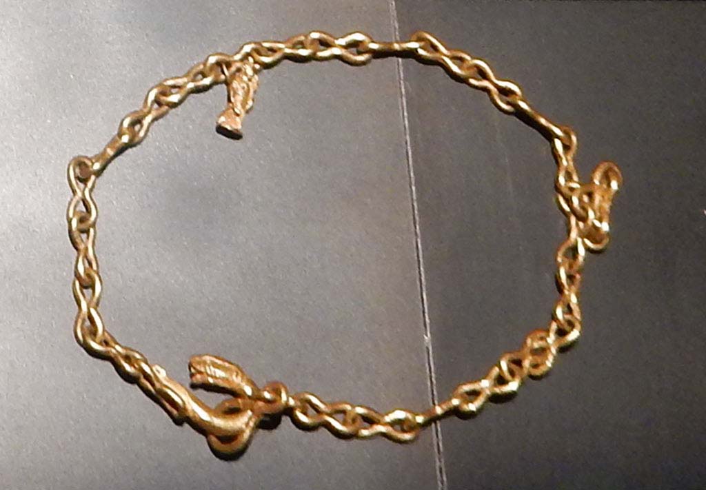 1.10.7 Pompeii, June 2019. 
Heavy gold chain with figure-of-eight links, snake head fastening and pendant featuring a statuette of Isis Fortuna, holding a rudder and cornucopia.
This was one of the jewels found in the atrium and in the tablinum.
On display in Palestra exhibition of jewellery entitled “Vanity, storie di gioielli dalle Cicladi a Pompei”, from 10th May 2019 to 5th August 2019.
SAP inventory number 5413. Photo courtesy of Buzz Ferebee.
See Guzzo, P.G. ed. (2003): Tales from an eruption – (Civale, A: The House of the Craftsman). Milan, Electa; (p.140-42)
