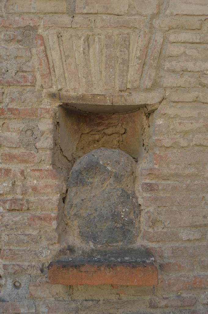 Street shrine or niche outside I.12.5 Pompeii. September 2005.
This is on Via dell’ Abbondanza, at the corner with Vicolo dei Fuggiaschi. 
According to Della Corte, on the red pilaster which ended the insula on the east side, two electoral programmes were found.
The first – 
GAVIVM II VIR.      [CIL IV 7442]
The second was immediately below the first - 
AMPLIATUM L F AED
                          VICINI                                                                                                           
                          SVRGITE ET
                           ROGATE
                           LVTATI F[ac]     [CIL IV 7443]
The text was placed towards the right, because the pilaster was interrupted in the middle by a rectangular niche.
In the niche was fixed a coarse rough stone resembling the outline of a human head, not the usual marble bust, as often seen here and there in the street.
See Notizie degli Scavi di Antichità, 1914, (p.204)
See Epigraphik-Datenbank Clauss/Slaby (www.manfredclauss.de).

According to PPM, inserted in the rectangular niche on the left side of the doorway was a blue lava stone, which had been a “lava-bomb” erupted during a prehistoric eruption and which was supposed to have been attributed with sacred and magical values. 
This was inserted into an apsed rectangular niche, with the lower level consisting of a tile projecting by about 6 cm and closed into the upper area by another tile with architrave under a flat arch in brick. 
See Carratelli, G. P., 1990-2003. Pompei: Pitture e Mosaici. Vol. II. Roma: Istituto della enciclopedia italiana. (p.736)

