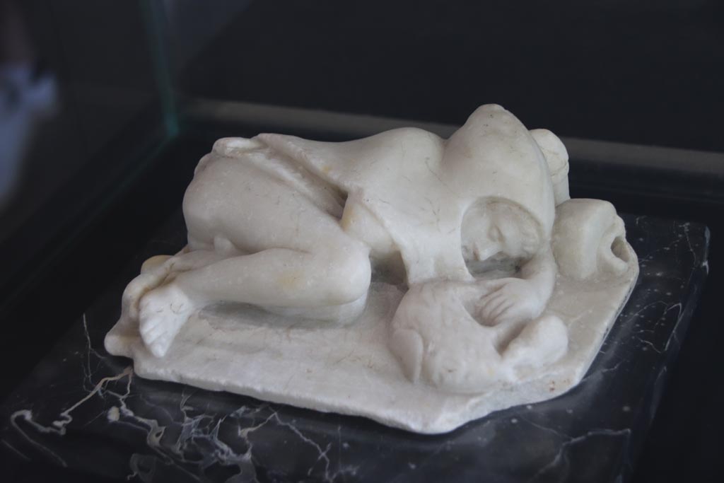 VI.2.22 Pompeii. October 2022. Marble statue described as “Young fisherman asleep”, found in the house but location unknown. 
On display in the Palaestra. PAP Inventory number 21628. Photo courtesy of Klaus Heese.
According to Jashemski –
“The two marble statuettes found in the house would probably have been garden decorations: a deer suckling her young (0.21m long) and a sleeping child whose left hand holds the handle of a basket which a mouse tries to enter. Behind the boy’s head an overturned vase (0.19m long) poured water.  The mask found in the house may also have decorated the garden.”
See Jashemski, W. F., 1993. The Gardens of Pompeii, Volume II: Appendices. New York: Caratzas. (p.122-3)
