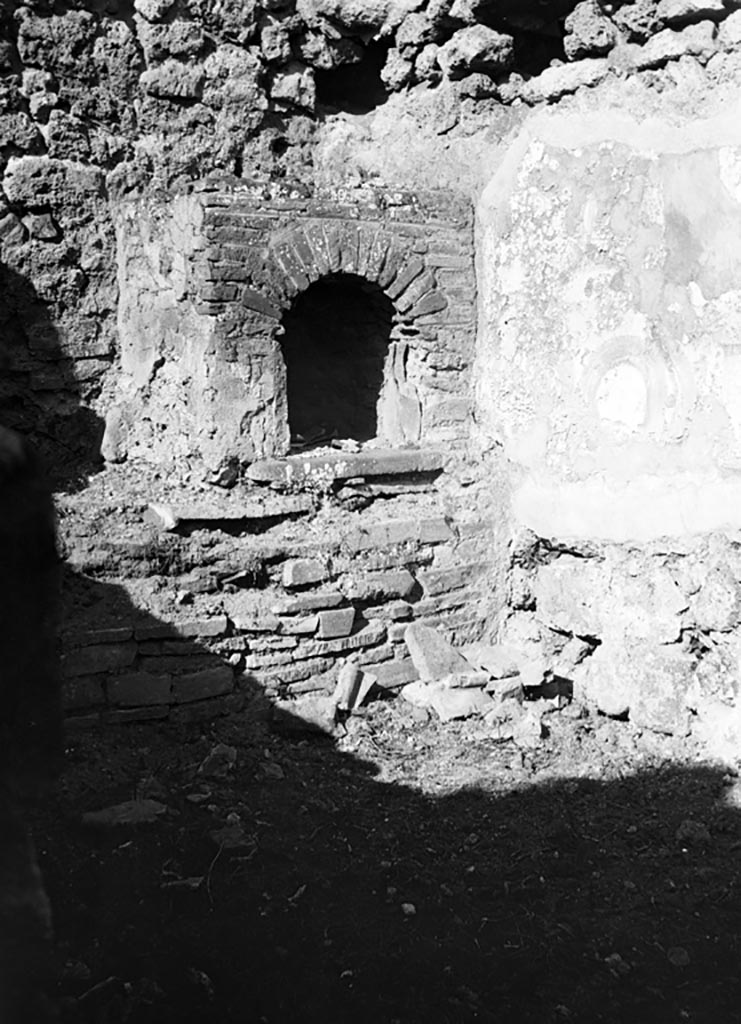 VI.7.7 Pompeii. December 2005. Kitchen, with bench and hearth against the west wall. According to Boyce, on the north wall of the kitchen was a lararium painting. Only a fragment was preserved, painted on a white background. In the centre was the Genius with a cornucopia and patera standing before a burning altar. Behind him was a camillus, above and behind the altar was the figure of the tibicen. On either side of this group stood the Lares in yellow tunic and green pallium. Beyond the Lar on the left was a small popa pushing a hog towards the right. The corresponding figure on the right of the right Lar was missing, as was the whole outer section of the plaster on this side. In the lower zone was the customary altar with the two serpents. See Boyce G. K., 1937. Corpus of the Lararia of Pompeii. Rome: MAAR 14. (p.47, no.163)
Boyce added a note that said Helbig (58) wrongly assigned this shrine to VI.7.9. See Helbig, W., 1868. Wandgemälde der vom Vesuv verschütteten Städte Campaniens. Leipzig: Breitkopf und Härtel. (58)
