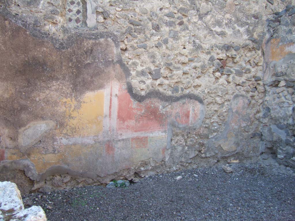 VI.13.2 Pompeii. September 2005. 
Remains of painted wall decoration on west wall of kitchen with latrine, and small window onto side roadway.
The yellow panelled zoccolo was separated by narrow red compartments.
In the middle zone of the wall the yellow and red panels were separated by narrow black (now discoloured) compartments, crossed by a small column with ribbon decorations.
