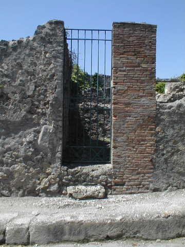 Lead pipe in pavement between VI.15.3 and VI.15.4 on Vicolo dei Vettii.  
The pipe goes through the wall of VI.15.4. December 2007.

