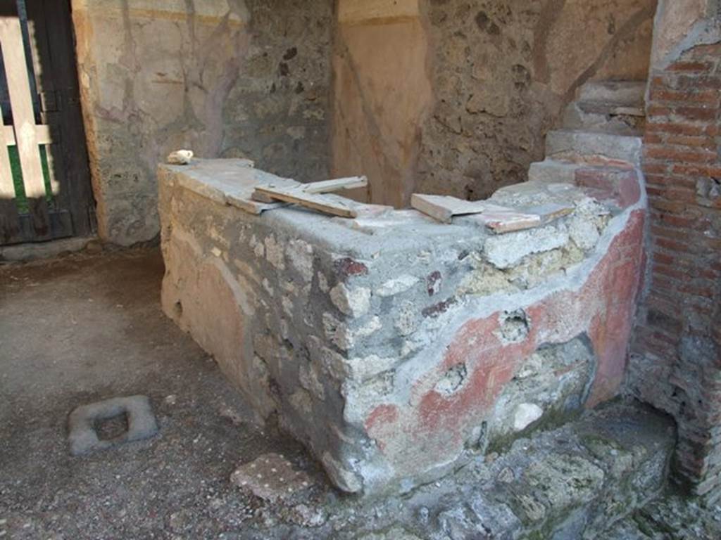 VI.16.33 Pompeii. December 2007. Two-sided counter next to south wall, with painted plaster with red background. According to NdS, the threshold of this wide doorway was missing, but it may have been made of wood on the side of the roadway. The floor was Opus signinum, buried in the floor near the entrance from the street was a piece of lava-stone with a hole in the middle for the closure bar.
