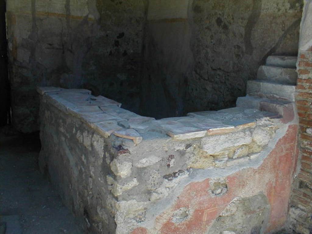 VI.16.33 Pompeii. May 2005. Two-sided masonry counter, and shelving for display. These four small shelves, on the right, were made from masonry and were painted red. According to NdS, a painted figure was seen at the extreme end of the counter, on the left, in its north facing arm. This male figure was 0.57m high, with long yellow robe raised by his erect phallus. The same figure was painted opposite.
