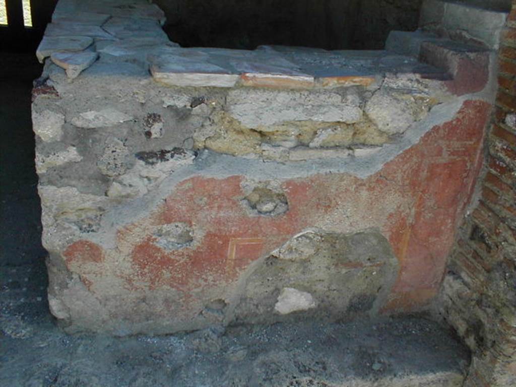 VI.16.33 Pompeii. May 2005. Remaining painted plaster on west-facing exterior side of counter. According to NdS, the outer surface of this counter had a red background. On the surface facing the road, according to Sogliano, obscene paintings were discovered. In the centre, in a yellow frame, was a large erect phallus. On each side, a male figure could be seen facing towards the centre panel and each other. The figure on the right was better preserved, and bald. There were also other painted panels and arabesques.See Notizie degli Scavi di Antichità, 1908, (p.289).
