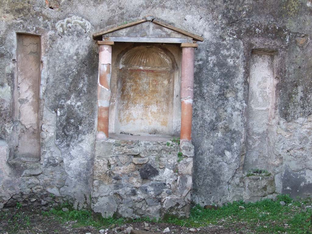 VII.3.6 Pompeii. December 2006. According to Boyce, above a rectangular podium stood two columns coated with red stucco.
These supported the roof with pediment. 
The semi-circular niche in the rear wall had its vaulted ceiling adorned with a stucco shell.
The walls of the niche were painted orange and on each side of the niche was a stucco pilaster.
A large marble statuette of Venus Anadyomene was found in the aedicula.
On either side of the aedicula are two long vertical slits, Fiorelli suggested they may have held candelabra.
See Boyce G. K., 1937. Corpus of the Lararia of Pompeii. Rome: MAAR 14.  (p. 63, no: 259 and pl. 36, 1)
