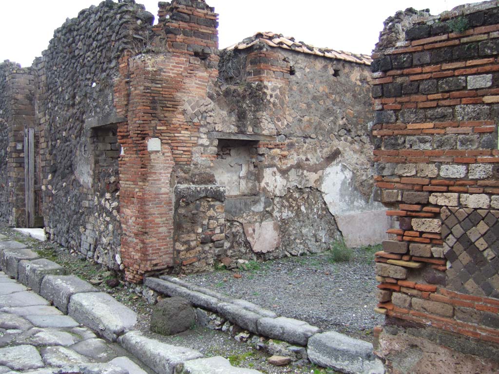 VII.10.2 Pompeii. December 2005. Entrance doorway on Vicolo d’Eumachia, looking north. 
According to Eschebach on the left of the entrance would have been the shop podium or counter, with shelves or steps above it.
See Eschebach, L., 1993. Gebäudeverzeichnis und Stadtplan der antiken Stadt Pompeji. Köln: Böhlau. (p.319)
According to Boyce, in the north wall was a large rectangular niche with a narrow shelf-like projection beside it on the left.
Fiorelli called it “un larario”.
Fiorelli, Descrizione, 273.
See Boyce G. K., 1937. Corpus of the Lararia of Pompeii. Rome: MAAR 14. (p.69, no.306).
