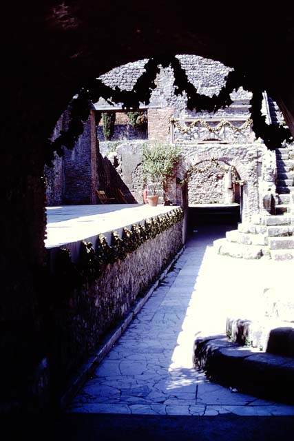 VIII.7.19 Pompeii.  May 2006.  East side with arched entrance. Above the entrances on either side were the rectangular areas which had the seats reserved for the honoured guests.  These were called the Tribunals. 
These were reached by the small narrow steps at the side, and separated from the rest of the audience by a sloping wall to the north.   The Kneeling Atlas and Lion’s foot were at the lower end of this sloping wall on both the West and East sides.
