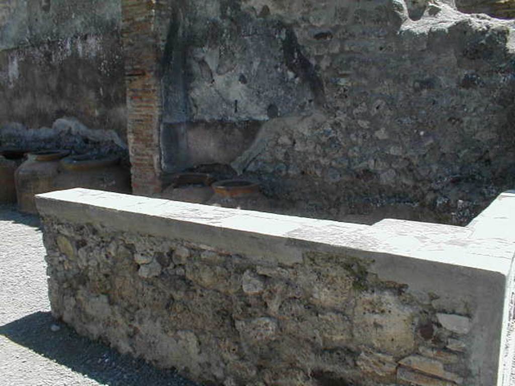 IX.1.3 Pompeii. May 2005. Marble counter. On the south wall of the shop, at the rear of the counter, the remains of the red painted zoccolo and white middle zone of the wall, can be seen.
