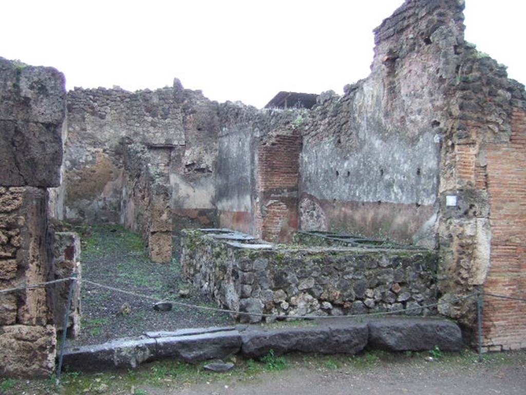 IX.1.8 Pompeii. December 2005. Looking east from Via Stabiana. The room at the front had a bench embedded with five large terracotta containers for provisions, support-holes for shelving for utensils, and a hearth on the north side near the doorway.  At the rear, (towards the east side), was a room possibly used as a dining room for the customers, as well as a narrow room where the stairs to the upper floor were found, underneath the stairs was the latrine.
