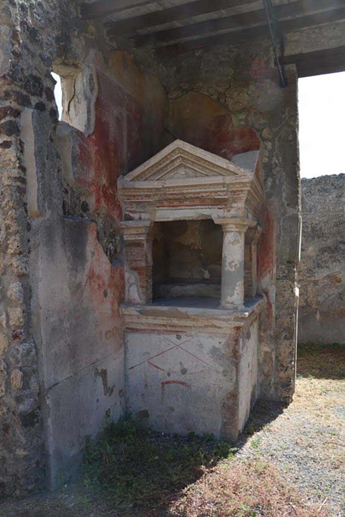 IX.1.22 Pompeii. December 2007.  Room 1, atrium with household shrine in south-east corner. According to Boyce, on the top of a high masonry podium stood the elaborately decorated aedicula.  The podium was decorated along the upper edge with a double band of painted stucco relief. There was one Doric column of heavy proportions with base and two rectangular pilasters attached to the room walls. These supported heavy entablature and cornice and a roof with two pediments. The cornices which surrounded the pediments were decorated with  uadruple bands of red and blue stucco relief.  The single column was also stucco coated and painted to imitate red and yellow marble. The walls, inside and out, were painted with decorations in red, green and yellow upon the white background; ornate portals, garlands, birds, candelabra and arabesques. Against the walls within the shrine was a low step, to serve as a pedestal for the figures of the gods.
See Boyce G. K., 1937. Corpus of the Lararia of Pompeii. Rome: MAAR 14. (p.80) 
