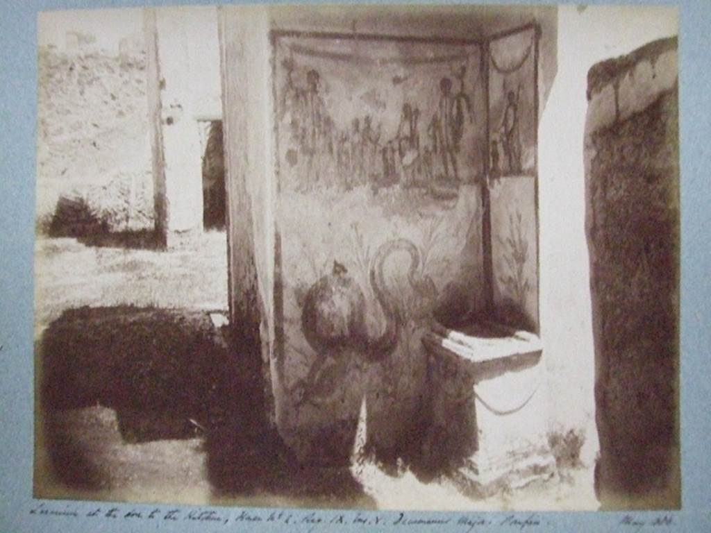 IX.5.2 Pompeii. Corridor w, lararium at the doorway to kitchen s and adjacent to entrance IX.5.22.
May 1886. Photograph courtesy of Society of Antiquaries, Fox Collection.
According to Boyce, the lararium was painted on two sides of a recess, each side bordered with red stripes.
In the centre on the east wall was an altar, between the Genius and two young men, apparently camilli.
On the left, behind the camilli, stood the tibicen, of smaller proportions than the other figures.
Behind the Genius was another Camillus, also small.
On each side of this group of five figures, stood a Lar, larger than the other figures.
Below this group, a bearded and crested serpent coiled towards the tufa altar in the corner of the east and south wall of the recess.
The tufa altar had been altered to fit into its new position in the corner, and then covered with a thick layer of stucco.
On the upper south wall of the recess, Vesta was painted, pouring a libation onto a yellow painted altar.
At her side stood an ass wearing a wreath of leaves. Vesta held a red halter attached to the asss muzzle.
Below Vesta was a single painted plant.
See Boyce G. K., 1937. Corpus of the Lararia of Pompeii. Rome: MAAR 14. (p.85, no.419, and Pl.16,2) 


