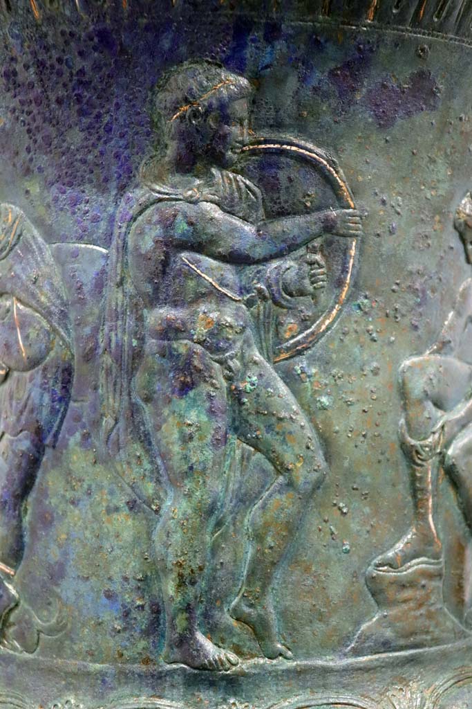 IX.13.1-3 Pompeii. February 2021. 
Bronze krater with scenes in relief, found in triclinium, on display in Antiquarium, VIII.1.4.
Detail of the young man holding a shield. Photo courtesy of Fabien Bièvre-Perrin (CC BY-NC-SA).

