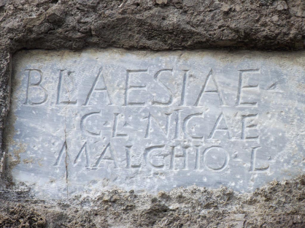 FPNH Pompeii. December 2005. Light blue marble plaque on west end of south side with inscription..

According to D’Ambrosio and De Caro, this read

BLAESIAE G. L. QVARTAE

They expand this to

Blaesiae
G(aiae) l(ibertae, Quartae

See D’Ambrosio A. and De Caro S., 1988. Römische Gräberstraßen. München: C.H.Beck. p. 212-3.
