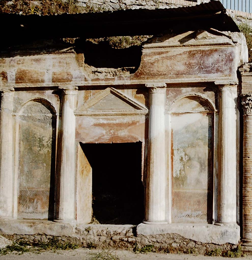 Pompeii Porta Nocera. 1959. Tomb 19ES. Richly decorated front of tomb with four columns, two top pediments, a lunette and stucco bordered panels. 
The front is richly decorated with garden paintings showing fences, marble crater fountains and shrubbery at the top of which are birds. 
Above the columns and below the top pediments are alternating and connected spirals of clovers and palmettes on a red background.
See DAmbrosio, A. and De Caro, S., 1983. Un Impegno per Pompei: Fotopiano e documentazione della Necropoli di Porta Nocera. Milano: Touring Club Italiano. 19ES.
Detail from photo by Stanley A. Jashemski.
Source: The Wilhelmina and Stanley A. Jashemski archive in the University of Maryland Library, Special Collections (See collection page) and made available under the Creative Commons Attribution-Non-Commercial License v.4. See Licence and use details.
J59f0365

