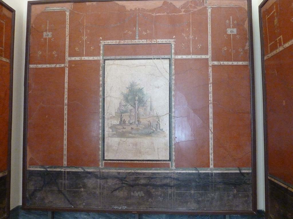 Villa Agrippa Postumus, Boscotrecase. May 2010. Room 16, north (rear) wall.
Now in Naples Archaeological Museum. Inventory number 147501.
A still-life depicting figs can be seen in the black ground dado/plinth of the rear wall. 
At the centre of the slender framed aedicule is a sacred landscape with shepherds and goats near a circular shrine and votive column, small panels with theatrical masks, delicate candelabra and branches with flowers complete the decorative ensemble in the upper zone.
