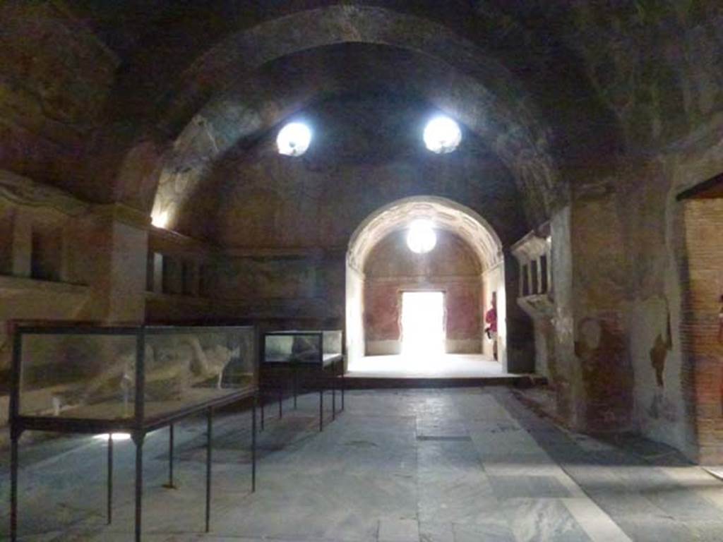 VII.1.8 Pompeii. June 2012. Looking west across apodyterium 2 towards vestibule 1 and entrance doorway from portico B. The doorway leading from the tepidarium 3 is on the near right. The doorway into frigidarium 4 is on the north side of vestibule 1, here seen with a figure standing in the doorway. Photo courtesy of Michael Binns.
