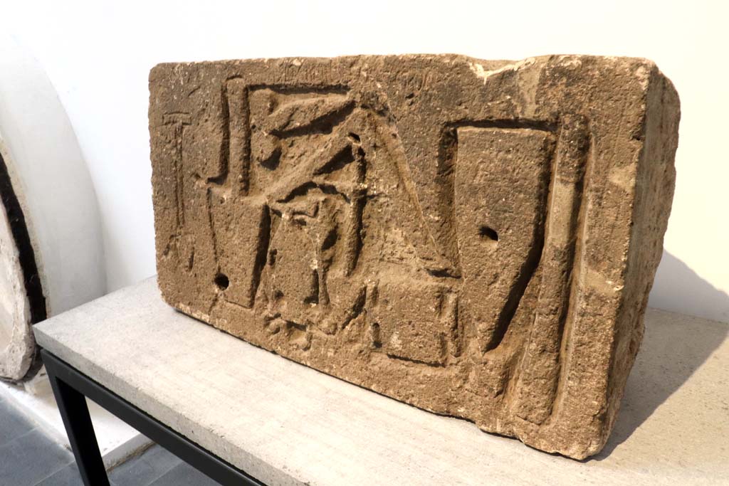 VII.15.1/2 Pompeii. February 2021. 
Limestone relief signed by the master builder (structor) Diogenes depicting –
a trowel, an apotropaic phallus, a plumbline, a cudgel or an axe/a hammer that cuts orthogonally, a scalpel and two unidentifiable objects. 
On display in Antiquarium at VIII.1.4, but found on the west perimeter wall of the house at VII.1.52, on Via dei Soprastanti.
Photo courtesy of Fabien Bièvre-Perrin (CC BY-NC-SA).
