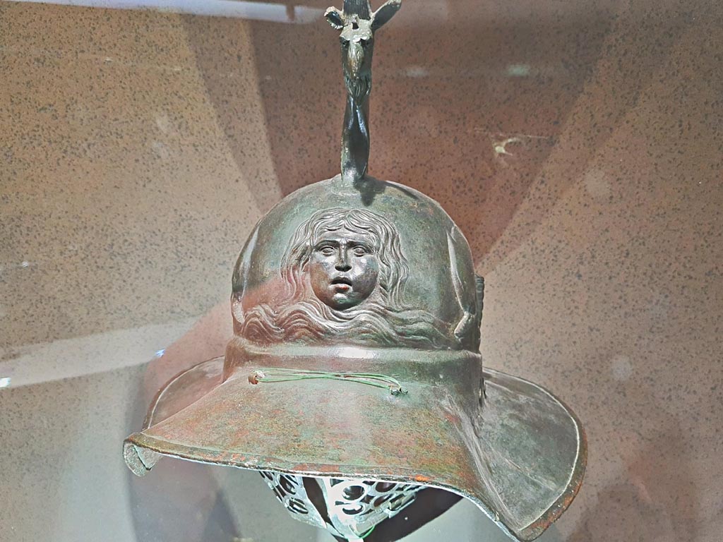 VIII.7.16 Pompeii. Gladiators helmet with depiction of a gorgon’s head. Photo taken May 2021, courtesy of Giuseppe Ciaramella.
This helmet belonged to a thraex, a gladiator armed like the Thracian warriors of south-eastern Europe.
The crest of this helmet ends in a griffin’s head and on the front, the helmet is decorated with a gorgon’s head, possibly Medusa.