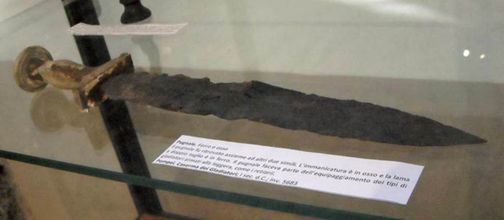 VIII.7.16 Pompeii. Gladiators dagger (pugnale) found in the Barracks with two other similar ones.
The handle is of bone and the blade is of iron and is double edged.
It was part of the equipment of a type of gladiator known as a retiarius (net fighter) who fought lightly armed.
Now in Naples Archaeological Museum. Inventory number 5683.