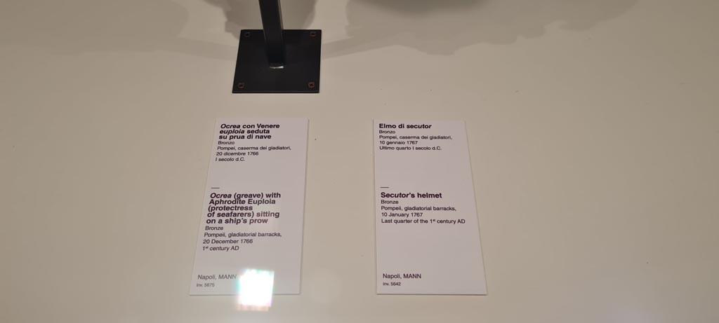 VIII.7.16 Pompeii. Description card for Secutor’s helmet and Aphrodite Euploia greave in Naples Archaeological Museum. Photo taken May 2021, courtesy of Giuseppe Ciaramella.