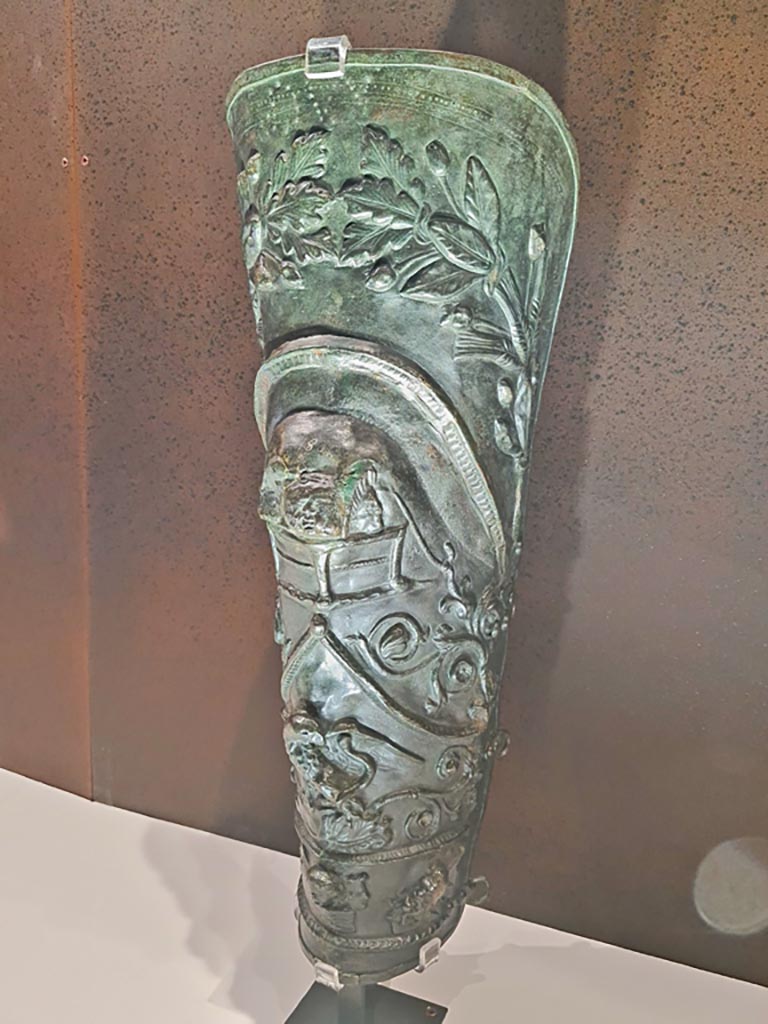 VIII.7.16 Pompeii. Photo taken May 2021, in Naples Archaeological Museum, inv. 5665.
Bronze greave depicting wheat ears, laurel and oak branches, masks and eagle fighting a snake.
Photo courtesy of Giuseppe Ciaramella.