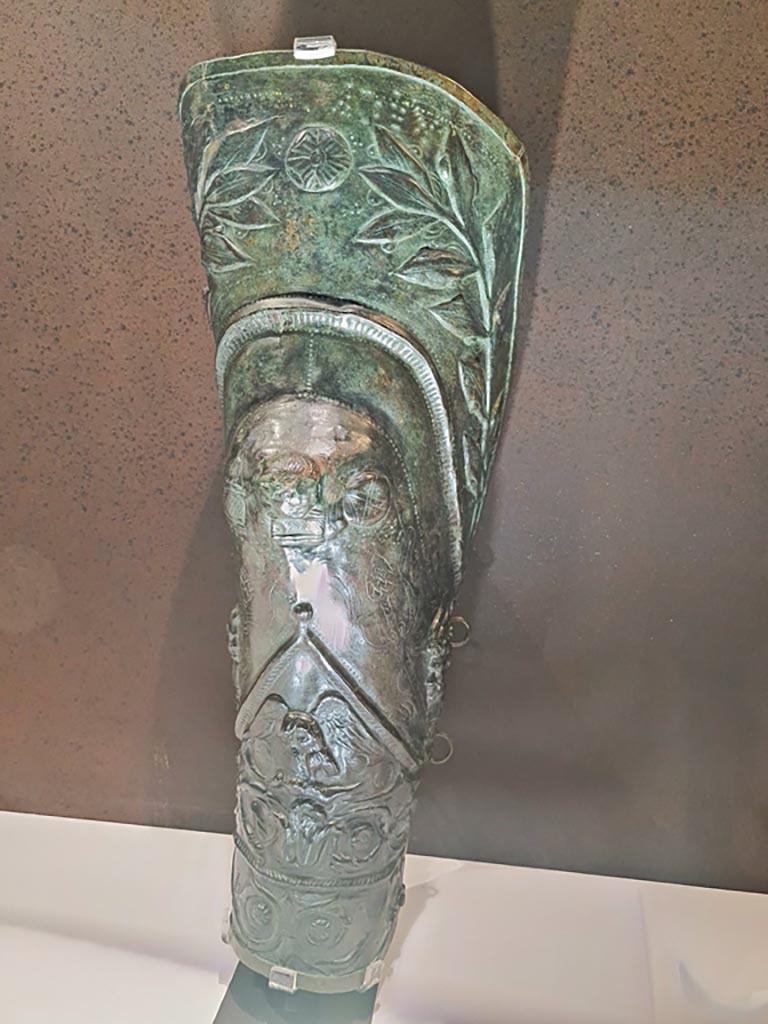 VIII.7.16 Pompeii. Photo taken May 2021, in Naples Archaeological Museum, inv. 5668.
Bronze greave depicting laurel branches, Bacchic masks, heads of Pan and an eagle clasping a hare.
Found 30th December 1766.
Photo courtesy of Giuseppe Ciaramella.