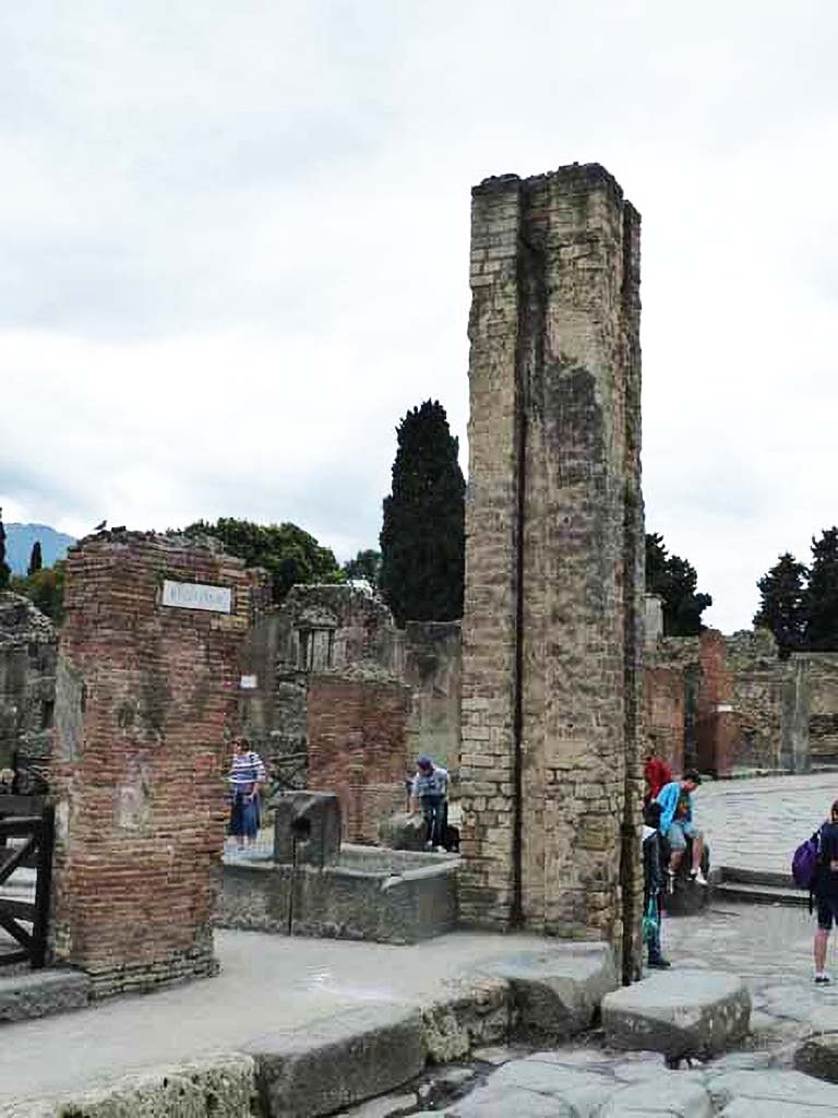 Via dell’ Abbondanza, south side, May 2010. 
Looking west to junction with Via Stabiana, and fountain and water column.
