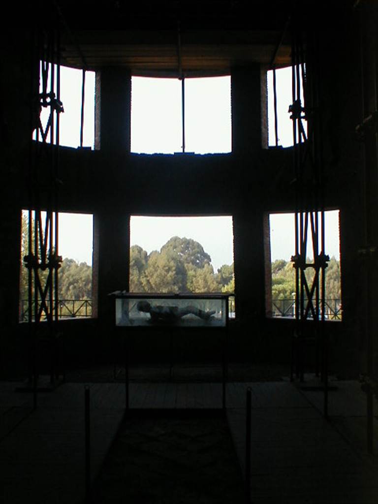 VII.16.17-22 Pompeii. September 2004. Looking west towards curved apse with six windows, in oecus.
A plaster cast, possibly of the uppermost victim, is on display in the case.
