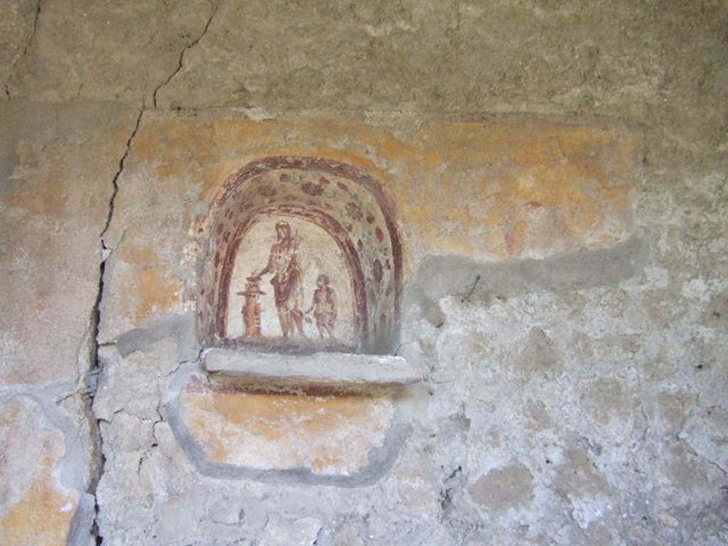 I.17.4 Pompeii. May 2006. Lararium niche on west wall of peristyle garden.  
A genius is making an offering at a round altar. A small camillus is to his left.
The side walls are painted with red flowers possibly roses.
On the yellow-coloured wall outside the niche, a colour trail is visible on the right, which perhaps belongs to a big snake. A paint ridge above the niche may perhaps be interpreted as a garland.
See Fröhlich, T., 1991. Lararien und Fassadenbilder in den Vesuvstädten. Mainz: von Zabern, L37, p. 264, taf. 9,1.
