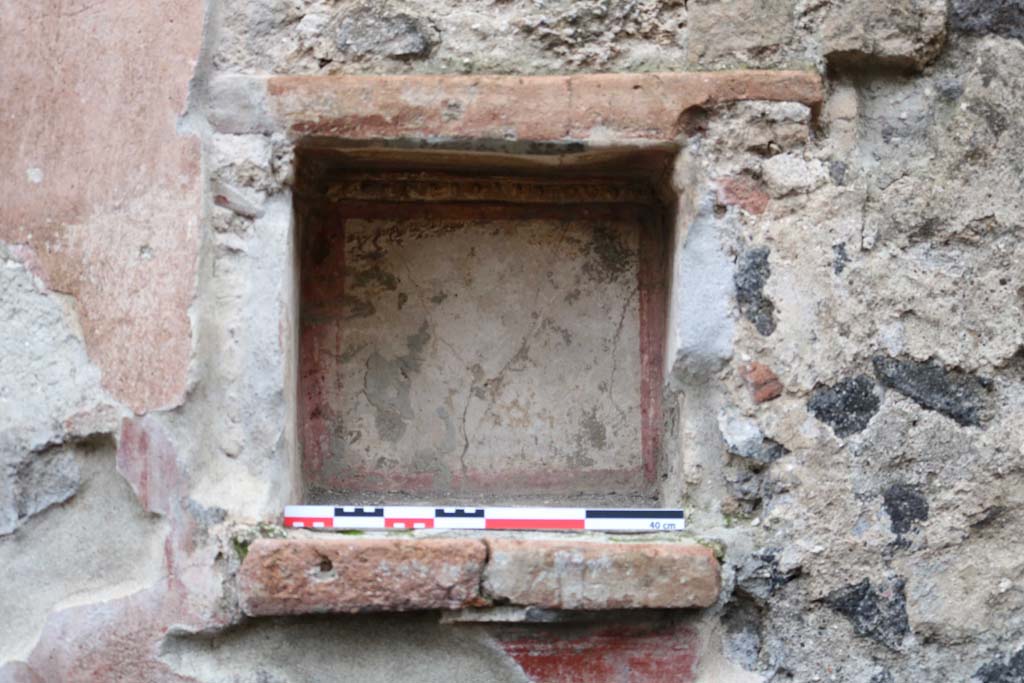 II.2.3 Pompeii. December 2018. Detail of east wall niche. Photo courtesy of Aude Durand. 
According to Boyce – 
In the east wall is a square nice (0.37 square, d.0.25, h. above floor 1.30) with heavy projecting ledge.
Its inside walls are white bordered in red, and around the top of them runs a stucco cornice with an ovolo in relief.
A similar cornice ran around three sides of the niche on the wall outside to judge from the one side where the plaster is preserved.
On the edge of the projecting shelf was a graffito – OLIVA CONDITA XVII K . NOVEMBRES
(Boyce notes that this graffito is discussed by Della Corte in Casa e Abitanti, in connection with No. 494). 
See Boyce G. K., 1937. Corpus of the Lararia of Pompeii. Rome: MAAR 14. (P.30, No.63).
