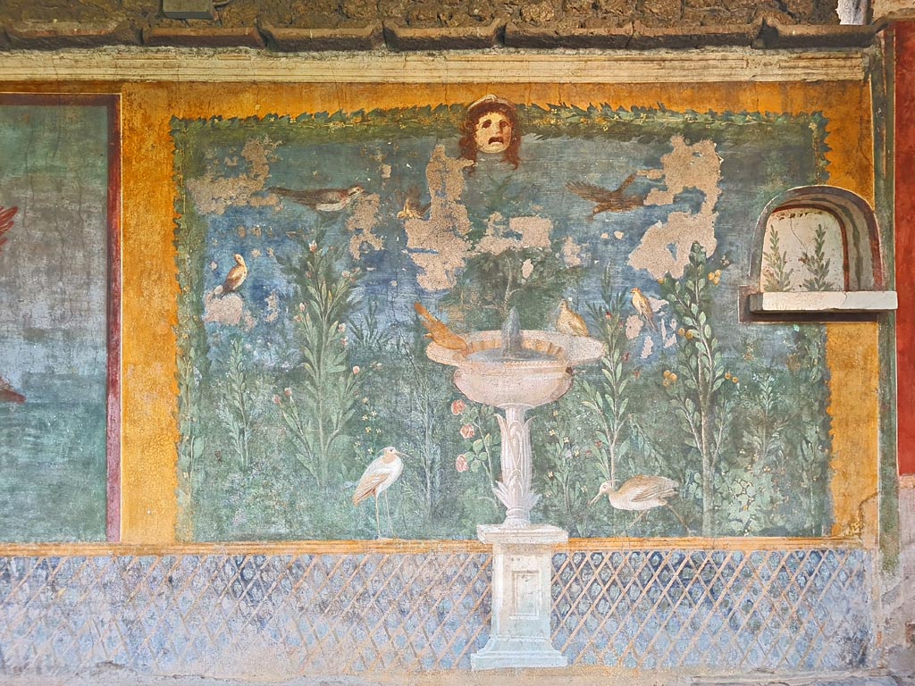 II.3.3 Pompeii. March 2024.
Room 11, west panel of south wall of peristyle with wall painting of fountain with garden, mask and birds. Photo courtesy of Giuseppe Ciaramella.
