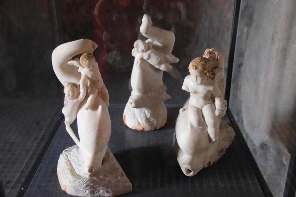 I.9.14 Pompeii. October 2022. 
Room 5, display cabinet with three of the four cupids, found in tablinum, room 6. Photo courtesy of Klaus Heese.

