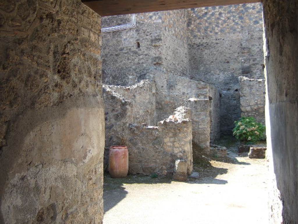 I.10.18 Pompeii. September 2005. Looking south-west from entrance fauces.
Right of centre is the area of room 6, looking ahead to cistern mouth in walkway No.8.
On the left at the end of the entrance corridor wall is the south-west side of the atrium.
Left of centre is room 7, the kitchen (room 9) is at the rear of room 7.

According to Boyce, in the south wall of the kitchen beside the hearth was a fragmentary painting in two zones.
It was on a white background outlined with red stripes.
In the upper zone stood the Genius, with a Lar.
In the lower zone, beneath garlands, was the tail of a black and yellow serpent.
Below the serpent were several kitchen articles, a hog’s head, a ham on a nail, and an eel on a spit.
See Notizie degli Scavi di Antichità, 1934, p. 344, and fig.38.
See Boyce G. K., 1937. Corpus of the Lararia of Pompeii. Rome: MAAR 14. (p.29, no.60) 
Fröhlich described it was “mostly fallen from the wall on the right but the left was mainly okay”.
See Fröhlich, T., 1991. Lararien und Fassadenbilder in den Vesuvstädten. Mainz: von Zabern. (L18, Taf. 26, 3)

