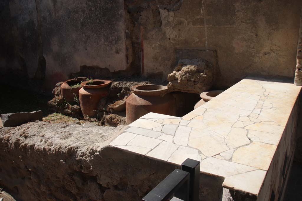 1.11.1 Pompeii. May 2015. Looking towards west side with remains of four urns and shelves for displaying drinking vessels.
Photo courtesy of Klaus Heese.

