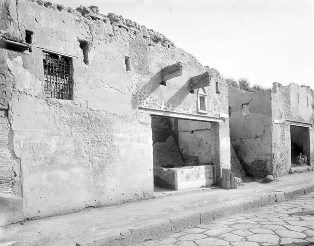I.11.1 Pompeii. Old undated photograph. Front wall with remaining graffiti on east side of entrance doorway, centre right.
Foto Taylor Lauritsen, ERC Grant 681269 DÉCOR.
According to Della Corte, on the wall between the doorways 1 and 2, high on the zoccolo, appeared the following programma, recommending C. Cuspio Pansa (written in black). 
