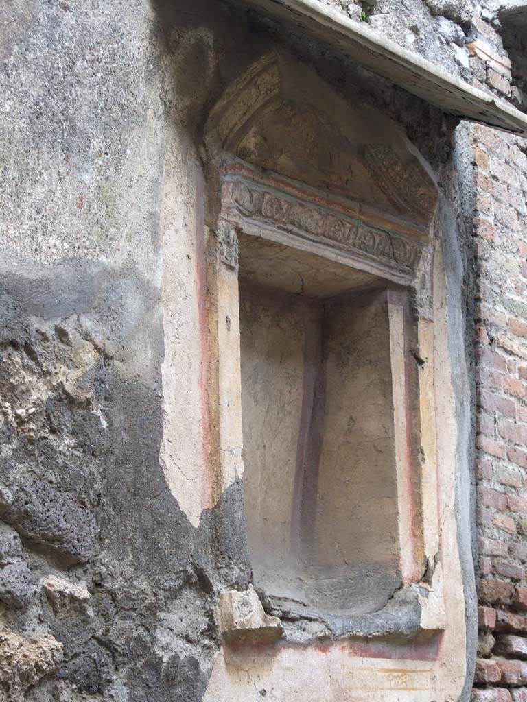 V.1.28 Pompeii. March 2009. Niche on north wall.
According to Boyce, the square niche was surrounded by an elaborate aedicula façade of stucco.
In the floor of the niche were holes for the bases of statuettes.
The niche and façade were brightly coloured, the rear wall was white bordered with red and having delicate painted green plants on it.
The pilasters of the façade were yellow, their capitals red, white and blue.
The bands of relief that ran around the architrave and the cornices were also painted in these colours.
On the wall below the niche was a painted band of yellow.
See Boyce G. K., 1937. Corpus of the Lararia of Pompeii. Rome: MAAR 14. (p.33, no.81, and Pl.1,5) 
See Giacobello, F., 2008. Larari Pompeiani: Iconografia e culto dei Lari in ambito domestico. Milano: LED Edizioni. (p.231)

