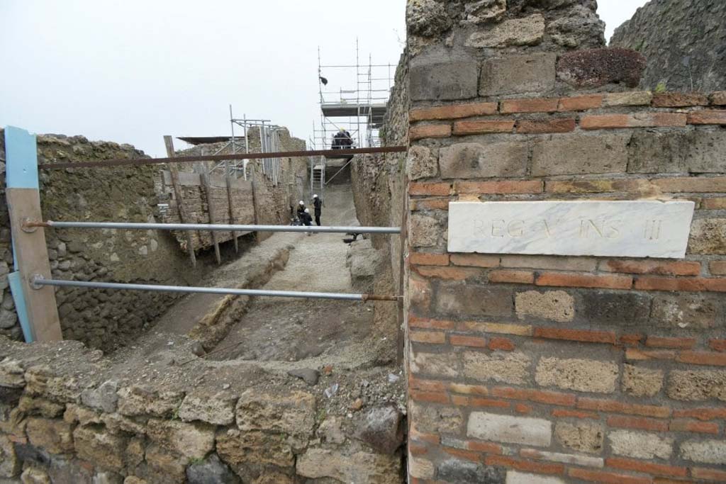 V.2.21 Pompeii. June 2018. Entrance to V.2.21 is still being excavated on the Vicolo dei Balconi past where the three people are.
